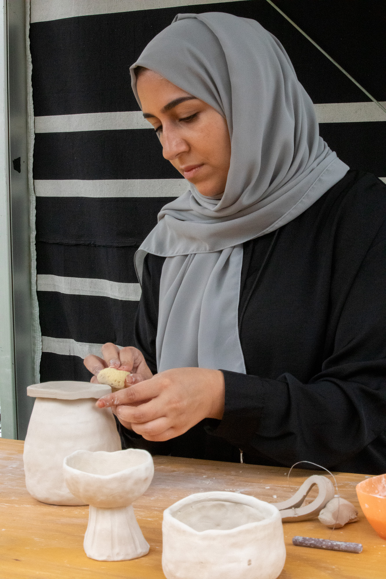 Woman using a small sponge to sculpt clay jar