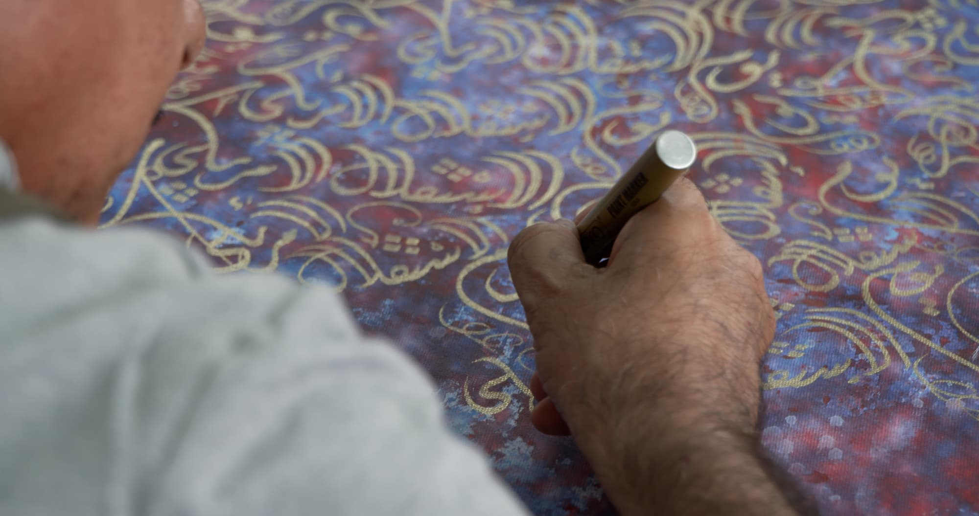 Close up photograph of Mohammed Mandi's hand as he writes with a gold marker