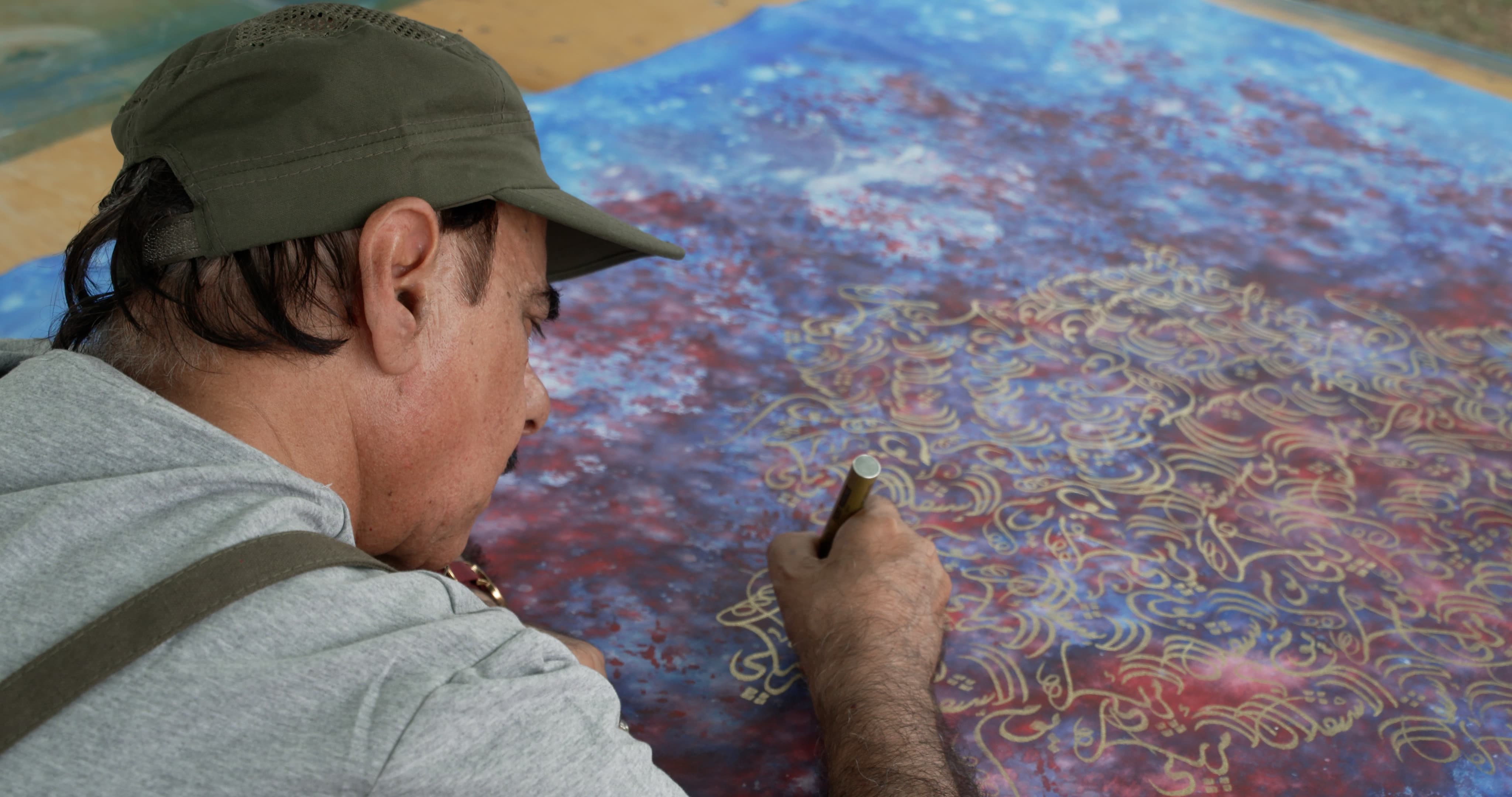 Over the shoulder angle of Mohammed Mandi as he writes calligraphy in gold ink