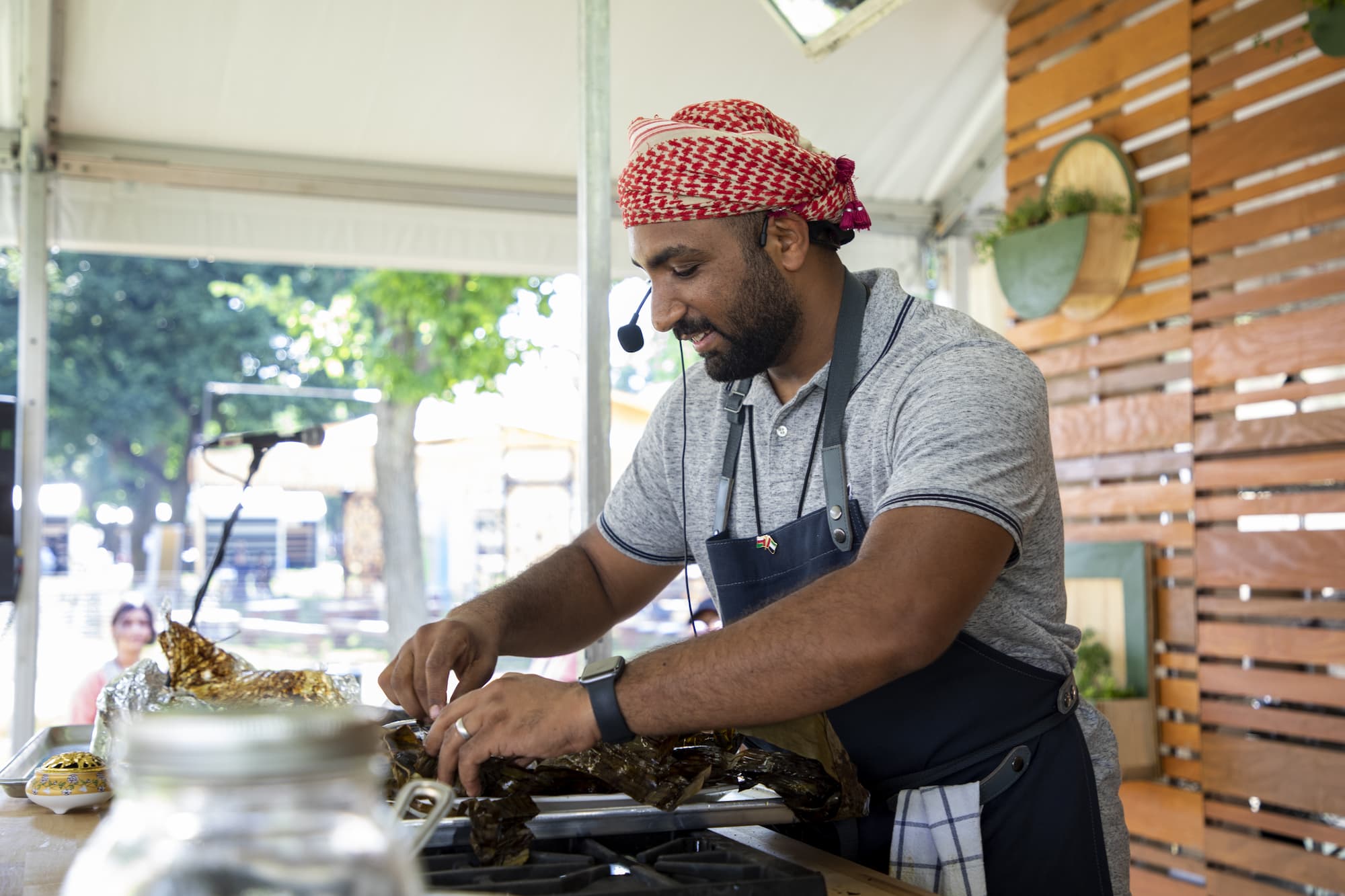 Mommin Al Rawahi smiling with a headset on stage as he unwraps a freshly cooked meal