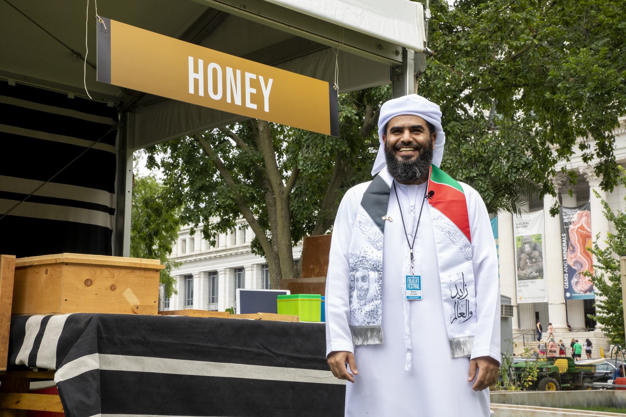 Manea Al Kaabi, smiling and standing in front of his honey booth