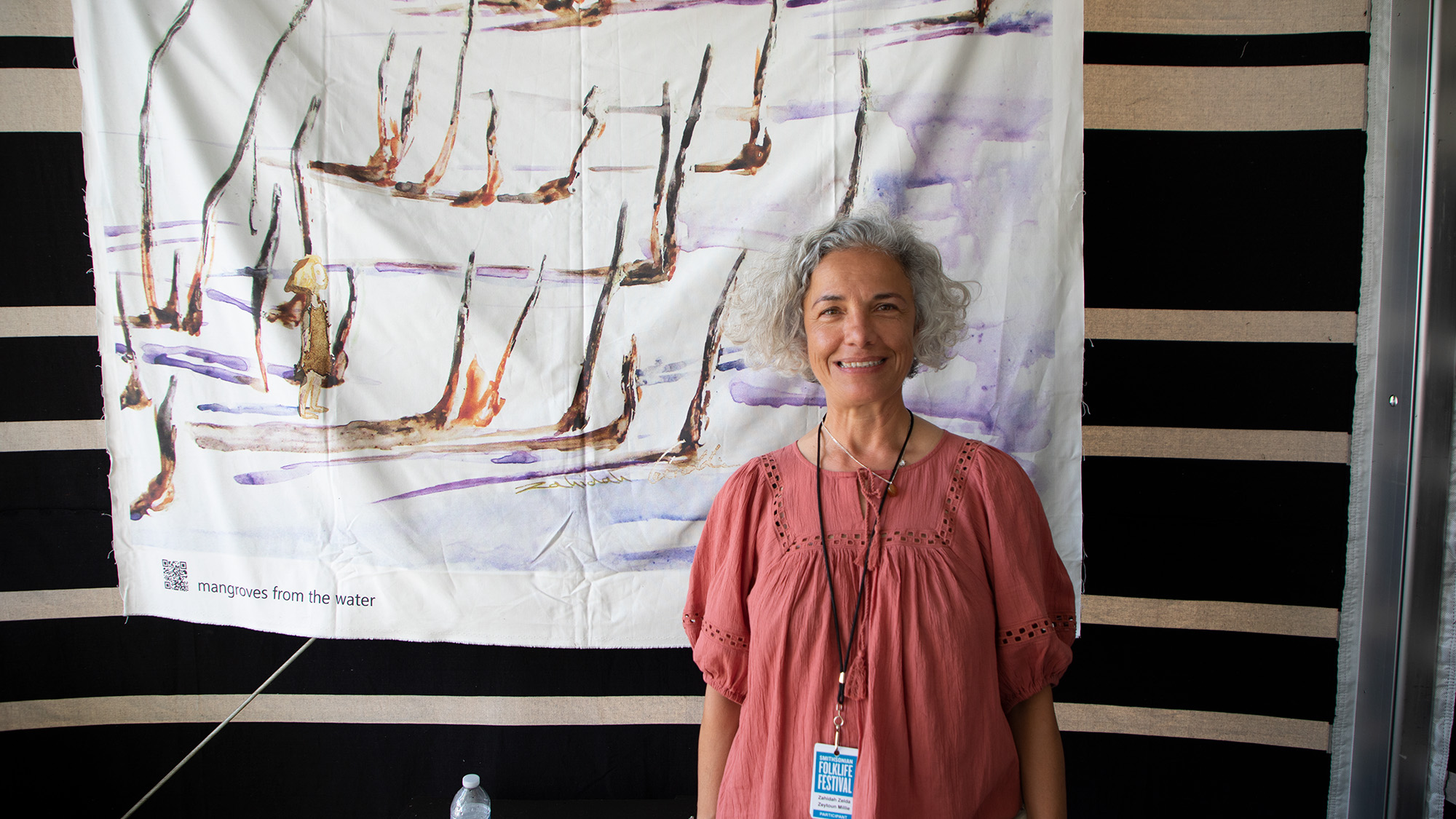 Zahidah Zeytoun Millie smiling in front of a large canvas that she painted with mangrove trees