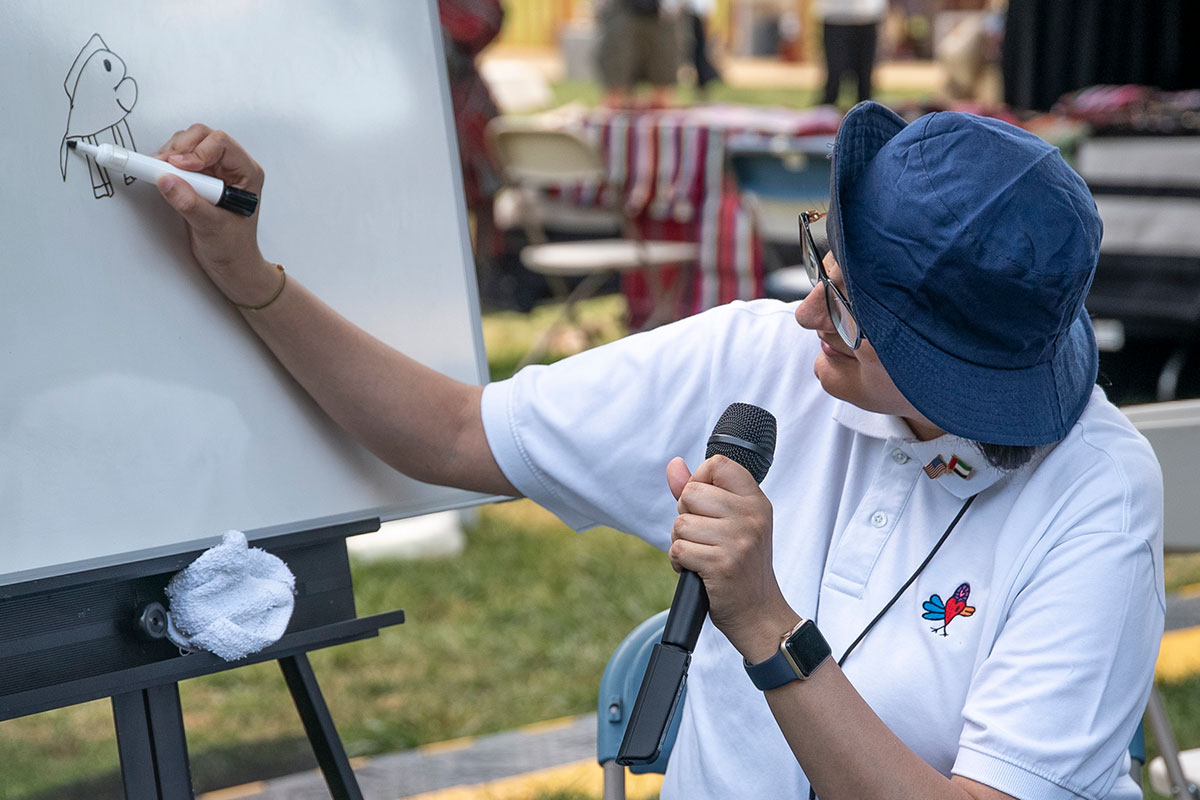 Woman wearing a blue bucket hat, drawing a cartoon on a white board