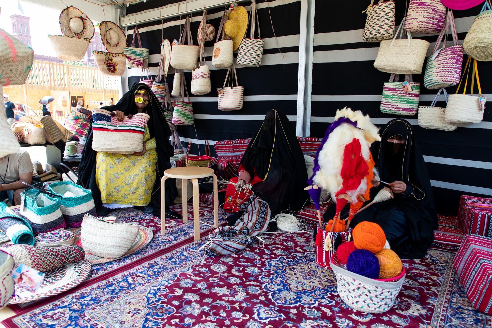 Three women sitting on a carpeted floor, surrounded by a large display of handwoven baskets