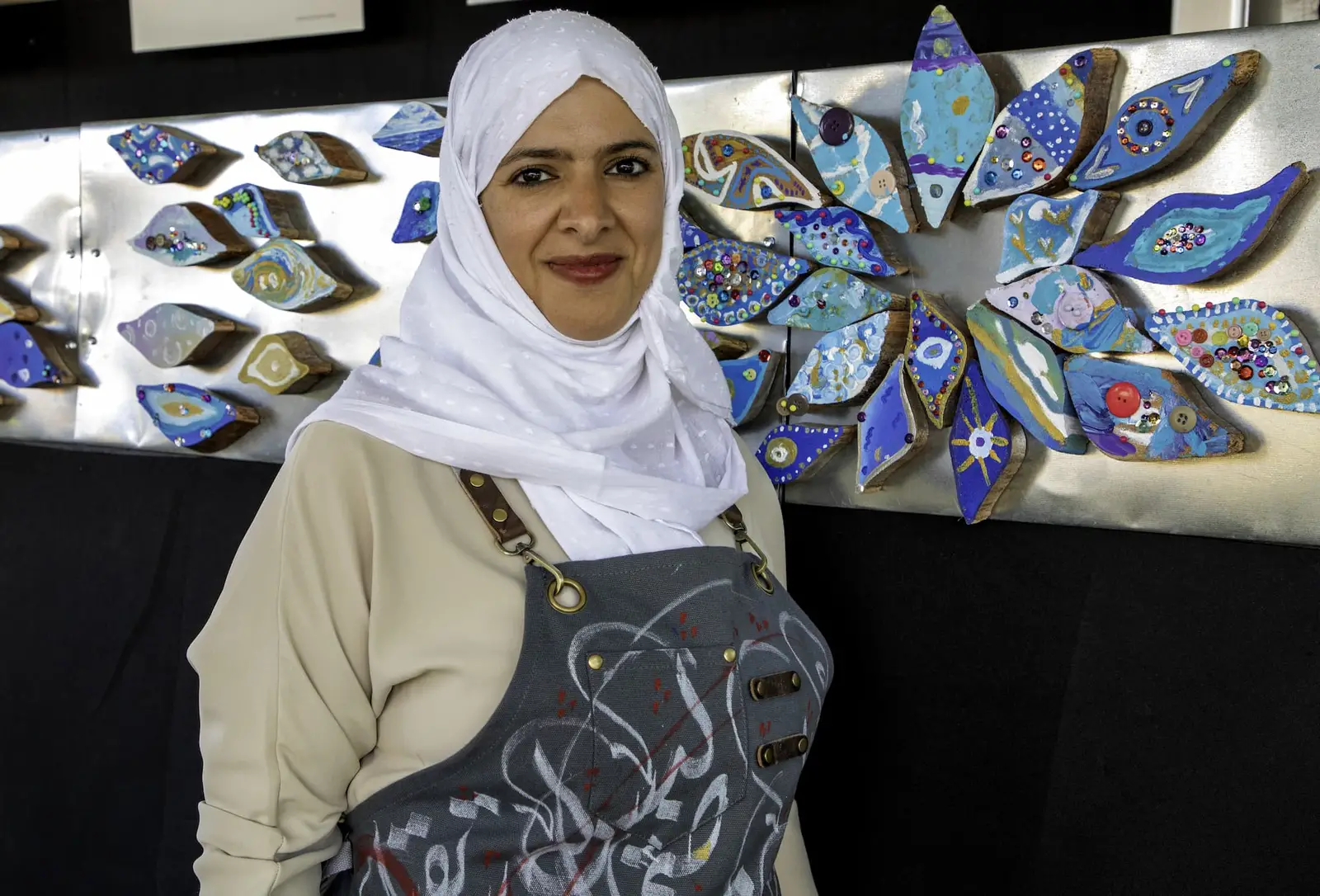 Women in a white head scarf and blue apron standing in front of an art display