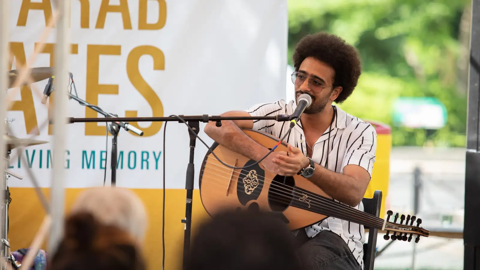 Man sitting in a chair on stage, singing into a microphone and playing acoustic guitar