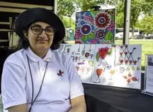 A woman wearing glasses and a hat sitting in front of an art display on an outdoor table