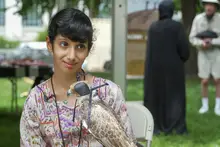 A young girl smiling and holding a live falcon on her arm