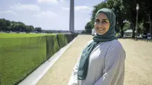 Smiling woman wearing a white top and teal headscarf standing on the National Mall in Washington, D.C., with the Washington Monument in the background